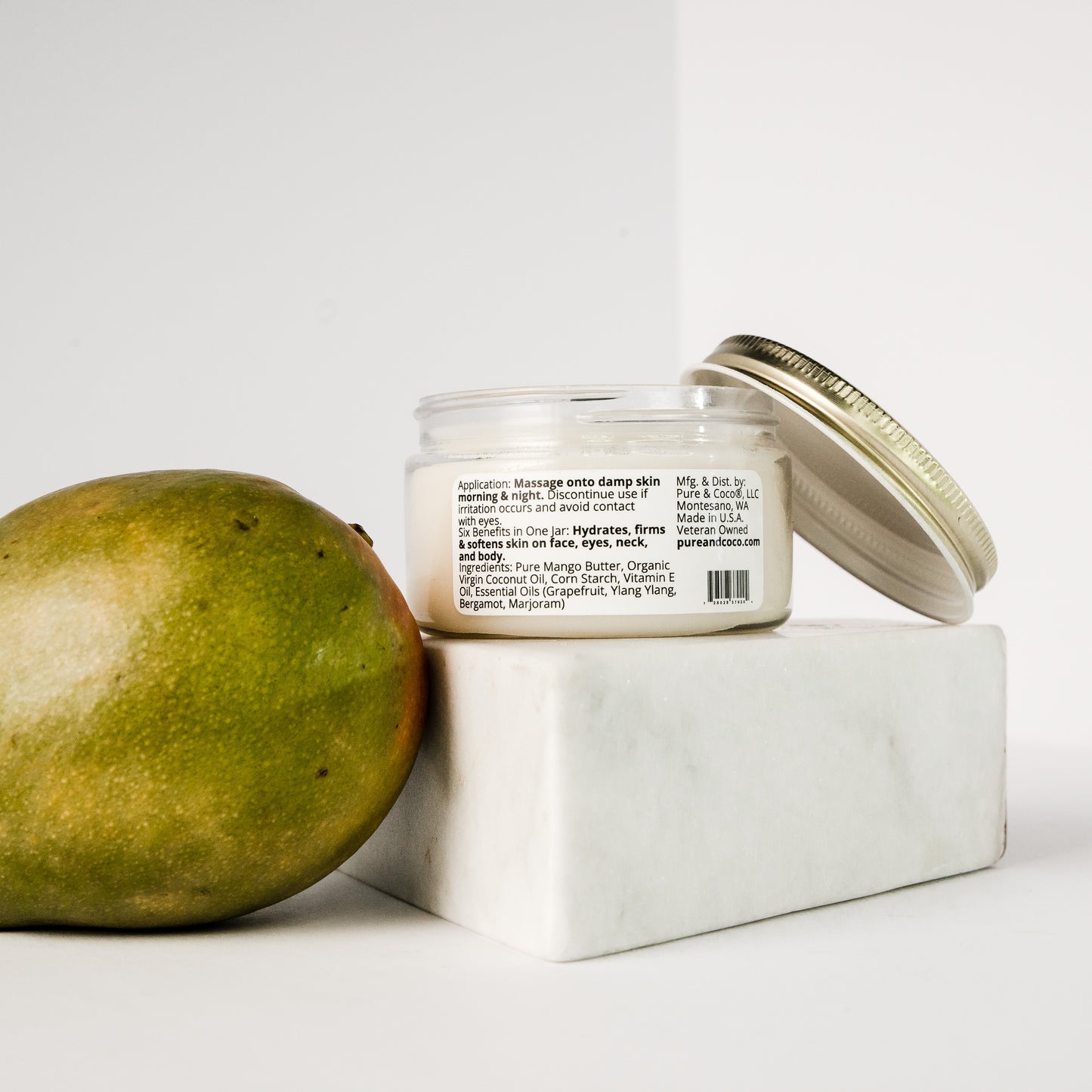 Ingredients shown for the Citrus Flora Mango Butter Face & Body Creme_4 oz_Pure and Coco sitting on a piece of marble with a mango sitting next to it
