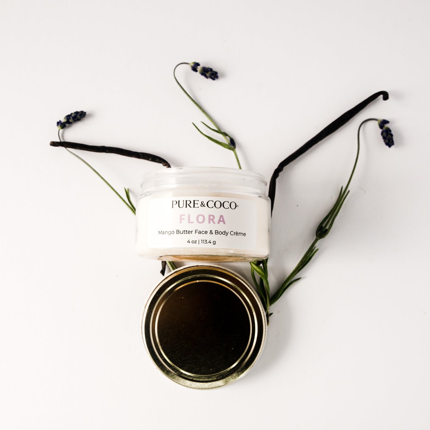 Flatlay of the Flora Mango Butter Face & Body Creme_4 oz_Pure and Coco with vanilla and lavender on a white background with the gold lid below