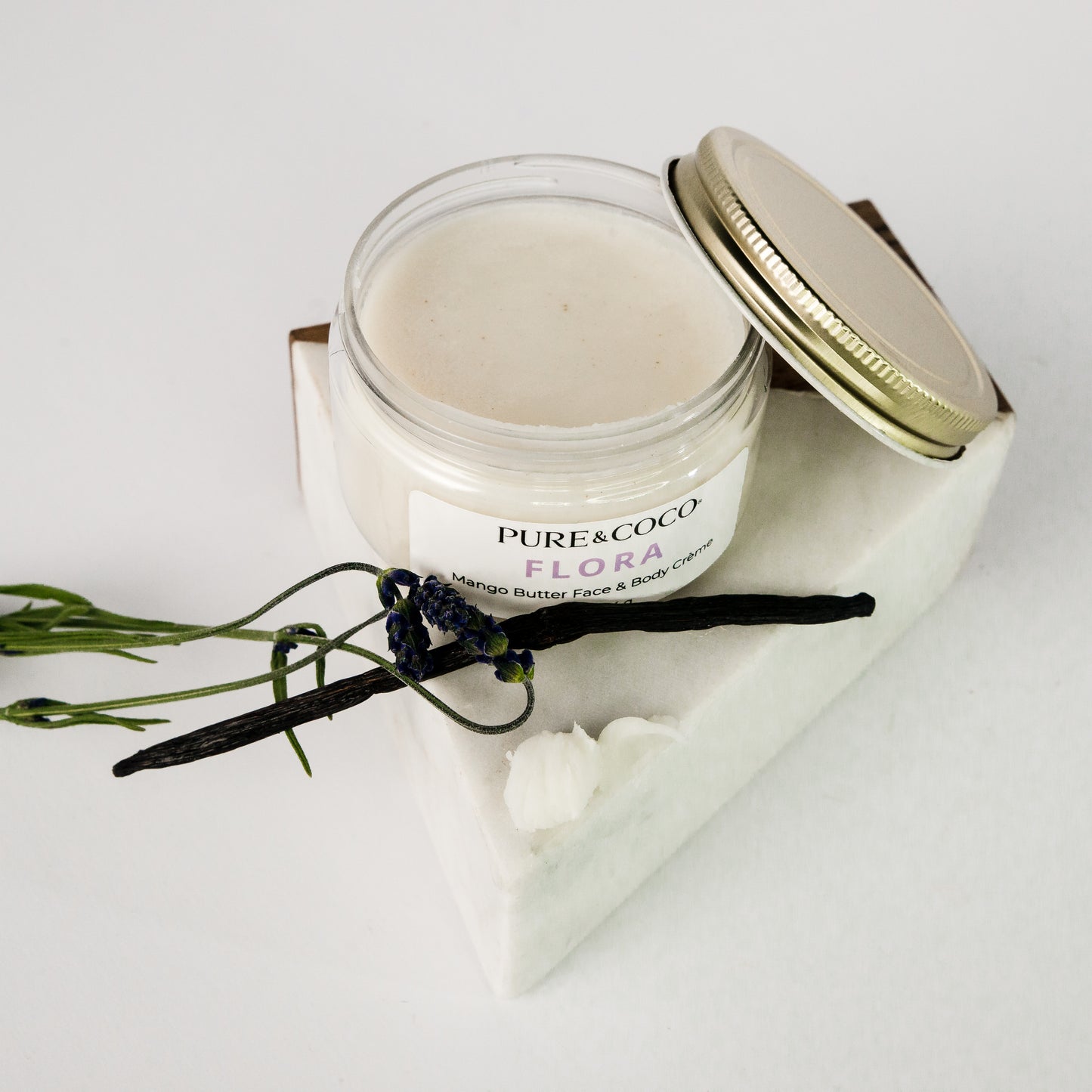 overlooking an open jar of the Flora Mango Butter Face & Body Creme_4 oz_Pure and Coco with the gold lid sitting proped up against the jar